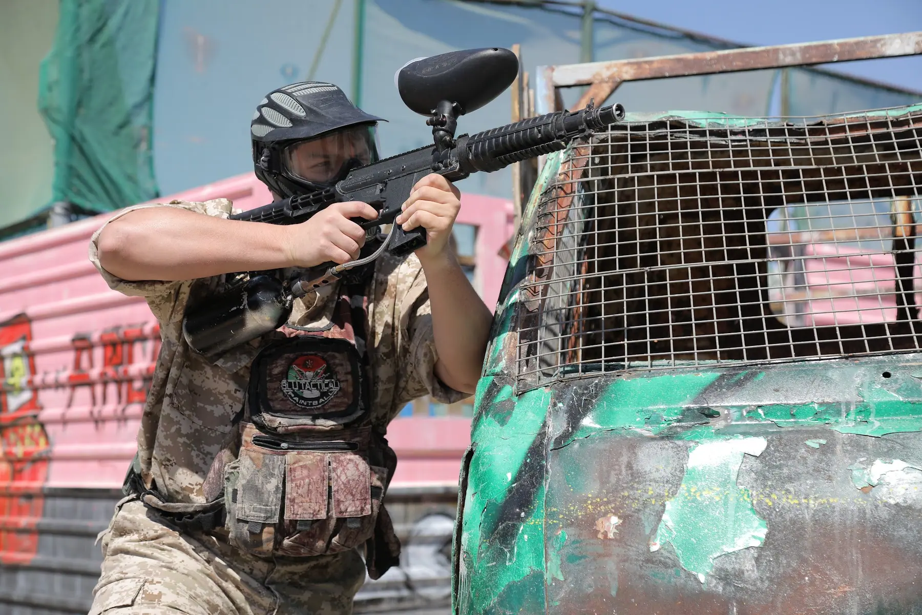 A BLU TACTICAL player aiming from behind a caged vehicle on the field